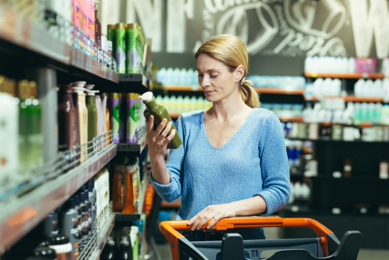 A woman stands in a store looking a a bottle in her hand,