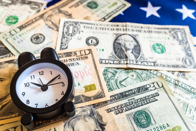 Alarm clock on dollar bills on top of the American flag.