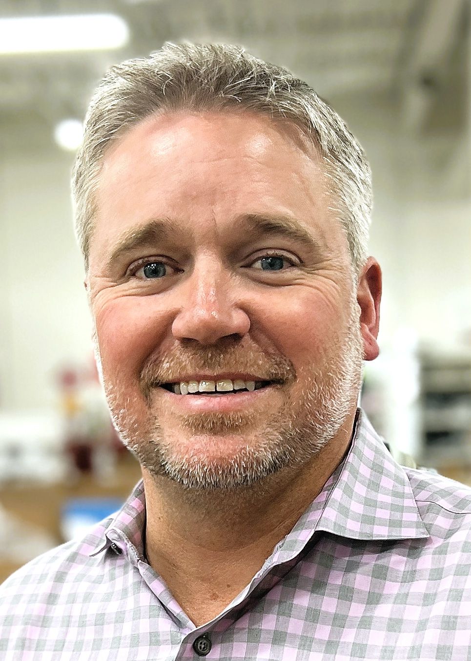 image of man with blonde hair and a very short beard wearing a checkered collared short with an office setting in the background