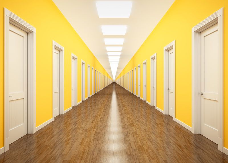 Image of a long corridor with bright yellow walls and white closed doors on each side running the length of the hall