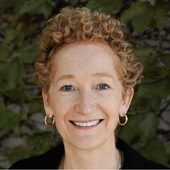 smiling woman with short red, curly hair wearing a black top with a beaded necklace outdoors