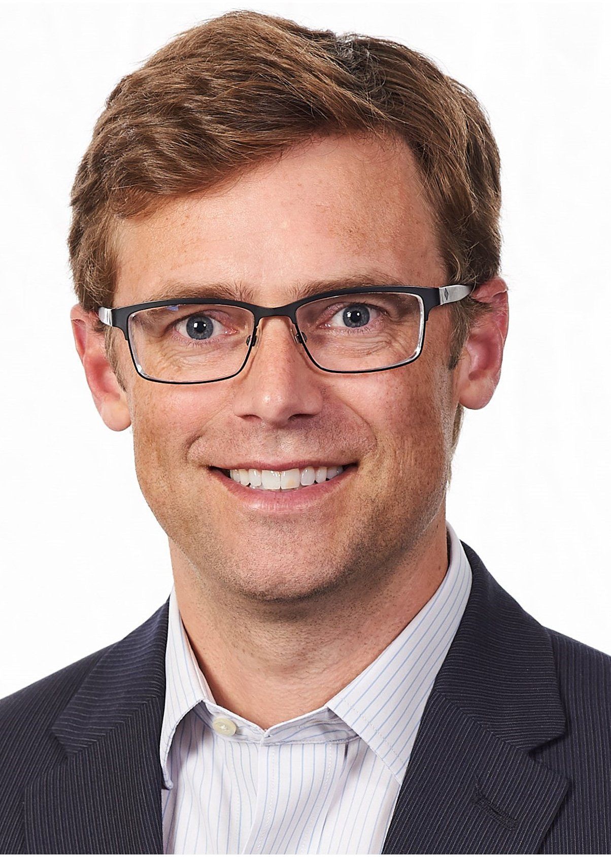 Image of a smiling man with light brown hair and with black rimmed eyeglasses and wearing a blue and white striped button up shirt and dark blue blazer